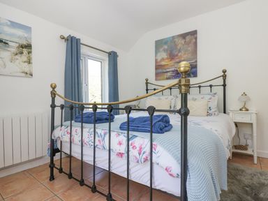 A bedroom with a black and brass metal bed frame with floral bedding and blue towels at Longships in Porthcurno