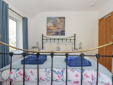 A bedroom with a metal bedframe a bed with floral bedding folded towels on the bed blue curtains wooden door and wall art at Longships in Porthcurno