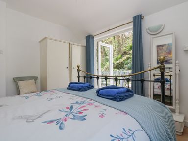 A bedroom with a bed having floral bedding and blue towels near a wardrobe and a full-length mirror at Longships in Porthcurno