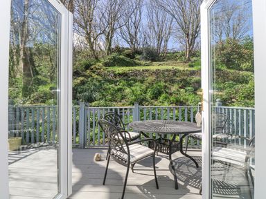 A patio with a round metal table and four chairs with cushions overlooking a hillside at Longships in Porthcurno