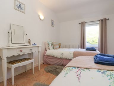 A bedroom with two single beds a vanity table with a mirror and a window with curtains at Longships in Porthcurno