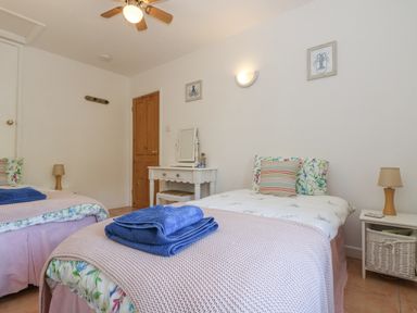 A bedroom with two single beds bedside tables with lamps a dressing table and wall art at Longships in Porthcurno