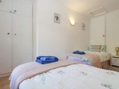 A bedroom with two single beds each with folded towels and floral bedding at Longships in Porthcurno