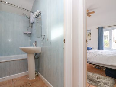 A bathroom with a pedestal sink and bathtub with shower next to a bedroom with a bed and window at Longships in Porthcurno