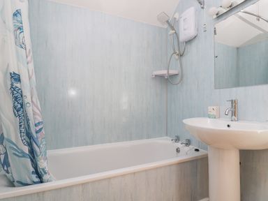 A bathroom with a bathtub shower unit curtain and a pedestal sink at Longships in Porthcurno