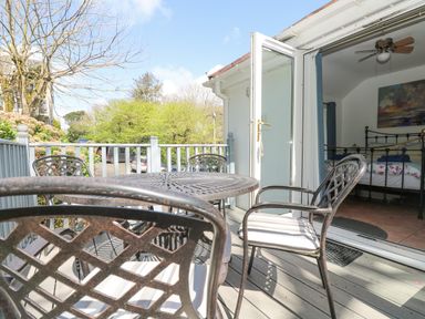 An outdoor patio with metal table and chairs next to an open door leading to a bedroom at Longships in Porthcurno