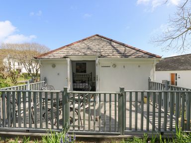 An outdoor patio with metal table and chairs leading to a room with a bed at Longships in Porthcurno