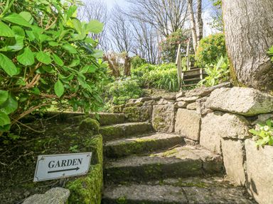 Stone steps with moss leading up in a garden with plants and a garden sign at Longships in Porthcurno