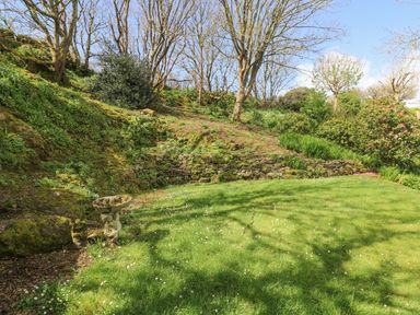 A garden area with grass trees shrubs and a bird bath at Longships in Porthcurno