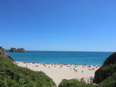 A sandy beach with people and umbrellas near the ocean and rocky cliffs at Longships in Porthcurno