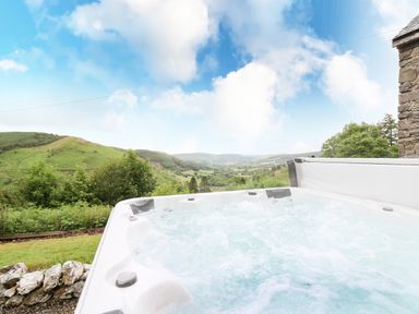 An outdoor hot tub with bubbling water overlooking green hills and trees at Pant Y Rhedyn in Abbeycwmhir near Rhayader