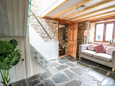 A living room with a gray sofa and cushions near a window a wooden door stone walls and floor at Pant Y Rhedyn in Abbeycwmhir near Rhayader