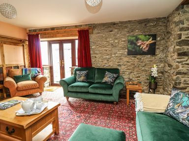 A living room with green and brown sofas a wooden coffee table a chess set and stone walls at Pant Y Rhedyn in Abbeycwmhir near Rhayader