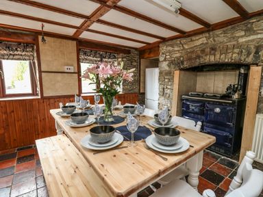 A dining area with a wooden table set for six with bowls glasses and napkins a vase with flowers a bench and chairs and a stove in a stone wall at Pant Y Rhedyn Abbeycwmhir near Rhayader