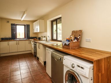 A kitchen with wooden countertops white cabinets a washing machine a dishwasher a fridge and a window with a basket on the counter at Pant Y Rhedyn in Abbeycwmhir near Rhayader