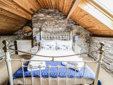 A bedroom with a metal bed frame stone walls wooden ceiling bedside tables with lamps and a chest of drawers at Pant Y Rhedyn in Abbeycwmhir near Rhayader