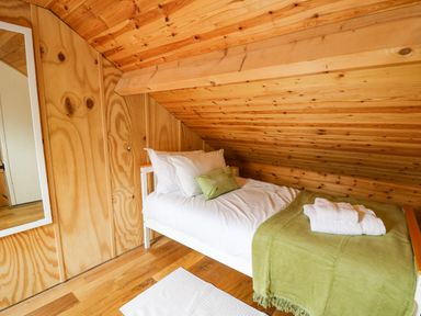 A small bedroom with a single bed covered with white bedding and a green throw under a slanted wooden ceiling with a mirror on the wall at Pant Y Rhedyn in Abbeycwmhir near Rhayader