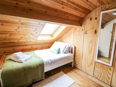 A small wooden bedroom with a single bed a green blanket folded towels a skylight and a wall mirror at Pant Y Rhedyn in Abbeycwmhir near Rhayader