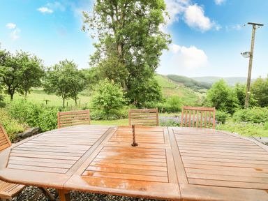 A wooden outdoor table and chairs with a natural landscape of trees and hills at Pant Y Rhedyn in Abbeycwmhir near Rhayader