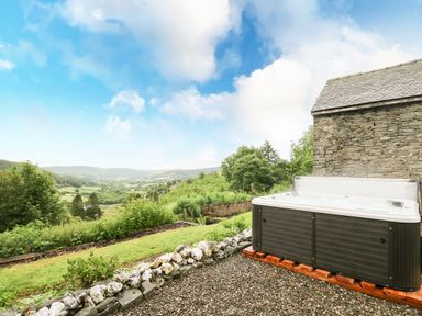 An outdoor hot tub next to a stone building overlooking a valley with trees and hills at Pant Y Rhedyn in Abbeycwmhir near Rhayader