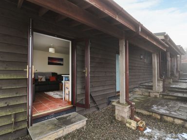 A patio with stone steps and a wooden exterior wall with an open glass door leading to a living room at Pant Y Rhedyn in Abbeycwmhir near Rhayader