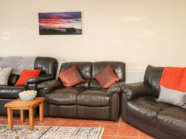 A living room with three dark brown leather sofas a wooden table with a bowl of popcorn and a landscape photo on the wall at Pant Y Rhedyn in Abbeycwmhir near Rhayader