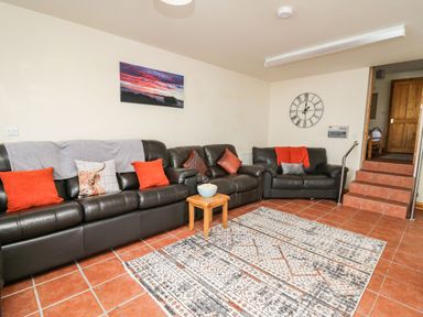 A living room with three black leather sofas a small wooden table with a bowl a large rug on tiled floor a wall clock and a photograph at Pant Y Rhedyn in Abbeycwmhir near Rhayader