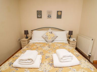 A bedroom with a bed with floral bedspread and two sets of folded white towels on it with two bedside tables and lamps Pant Y Rhedyn Abbeycwmhir near Rhayader