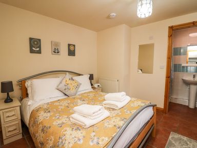A bedroom with a double bed with floral yellow bedspread and towels on it two bedside tables with lamps and wall art above the bed at Pant Y Rhedyn in Abbeycwmhir near Rhayader
