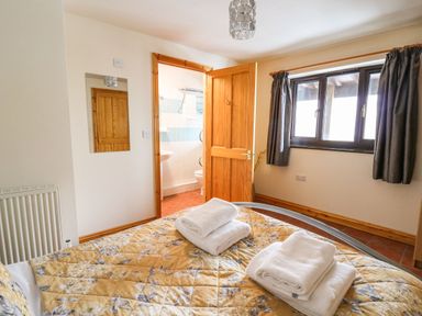 A bedroom with a bed covered in a yellow floral quilt and folded towels by a window and an open door leading to a bathroom at Pant Y Rhedyn in Abbeycwmhir near Rhayader