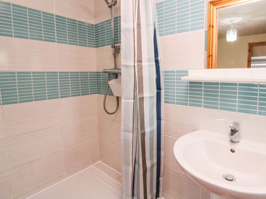 A bathroom with a shower area with striped shower curtain and a wall-mounted sink with a mirror at Pant Y Rhedyn in Abbeycwmhir near Rhayader