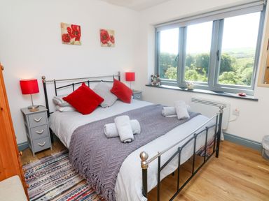 A bedroom with a double bed with cushions bedside tables with lamps a window with a countryside view at Higher Bumsley Barn in Parracombe