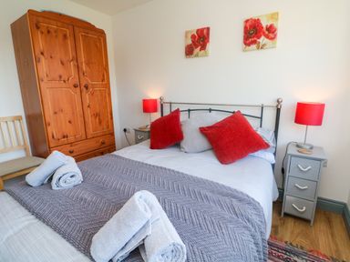 A bedroom with a double bed with red and gray pillows two bedside tables with lamps a wooden wardrobe and a chair at Higher Bumsley Barn in Parracombe