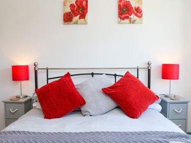 A bedroom with a bed with red and gray pillows red lamps on gray bedside tables and floral pictures on the wall at Higher Bumsley Barn in Parracombe
