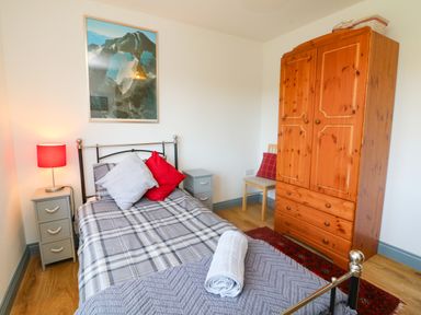 A bedroom with a single bed with pillows and a rolled towel bedside tables with a lamp a wooden wardrobe and a chair at Higher Bumsley Barn in Parracombe