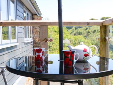 A glass outdoor table with two mugs and a teapot on a balcony with wooden railings at Higher Bumsley Barn in Parracombe