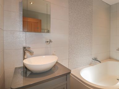A bathroom with a vessel sink on a countertop a wall mirror and a bathtub at Treetops in Otterburn