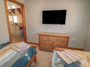A bedroom with two single beds and a wooden dresser with a mounted TV at Treetops Otterburn