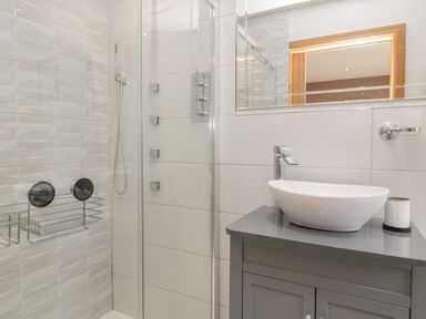 A bathroom with a glass shower enclosure and a white vessel sink on a grey cabinet at Treetops in Otterburn