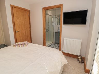 A bedroom with a bed and folded towels near two wooden doors a wall-mounted TV radiator and a stuffed animal at Treetops in Otterburn