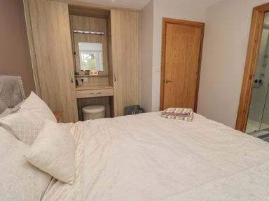 A bedroom with a bed covered in white bedding pillows a wooden wardrobe with a built in mirror and stool a wooden door and an open doorway showing a bathroom at Treetops in Otterburn
