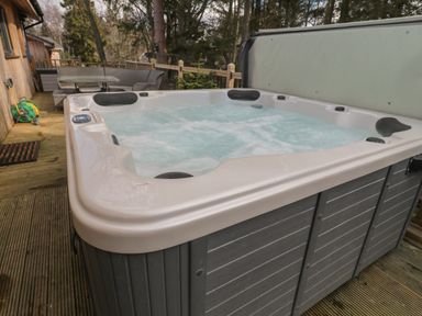 An outdoor hot tub on a wooden deck with patio furniture and trees in the background at Treetops in Otterburn
