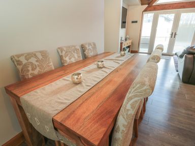 A dining area with a wooden table covered by a table runner and six upholstered chairs at Treetops Otterburn