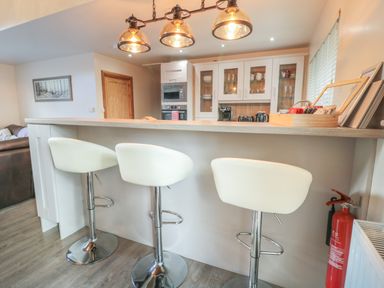 A kitchen with three white bar stools a wooden countertop and a fire extinguisher at Treetops in Otterburn
