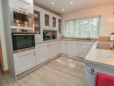 A kitchen with white cabinets a built-in oven microwave coffee machine kettle and a window with blinds at Treetops in Otterburn