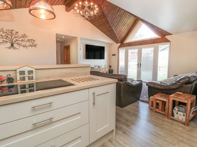 A living room with brown leather sofas and wooden tables near glass doors under a wooden vaulted ceiling at Treetops in Otterburn