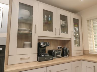 A kitchen countertop with a coffee machine toaster and kettle under glass cabinets with dishes at Treetops in Otterburn