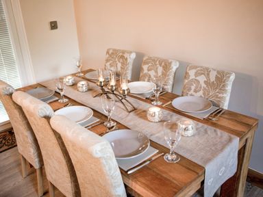 A dining table set with six chairs plates glasses and candles at Treetops in Otterburn