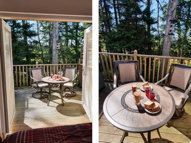 A small outdoor wooden deck with two chairs and a round table set with drinks and sandwiches at Treetops in Otterburn