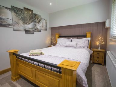 A bedroom with a wooden bed frame and bedside tables with lamps at Treetops in Otterburn